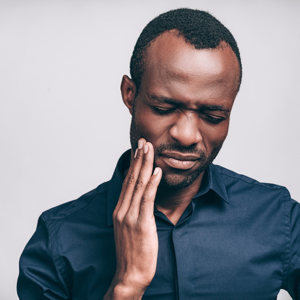 Feeling toothache. Frustrated young African man touching his cheek and keeping eyes closed while standing against grey background