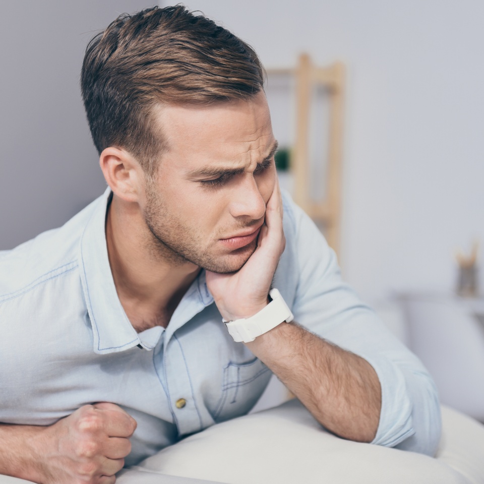Need a doctor. Handsome young unhappy man closing his eyes and having toothache while sitting in the room.