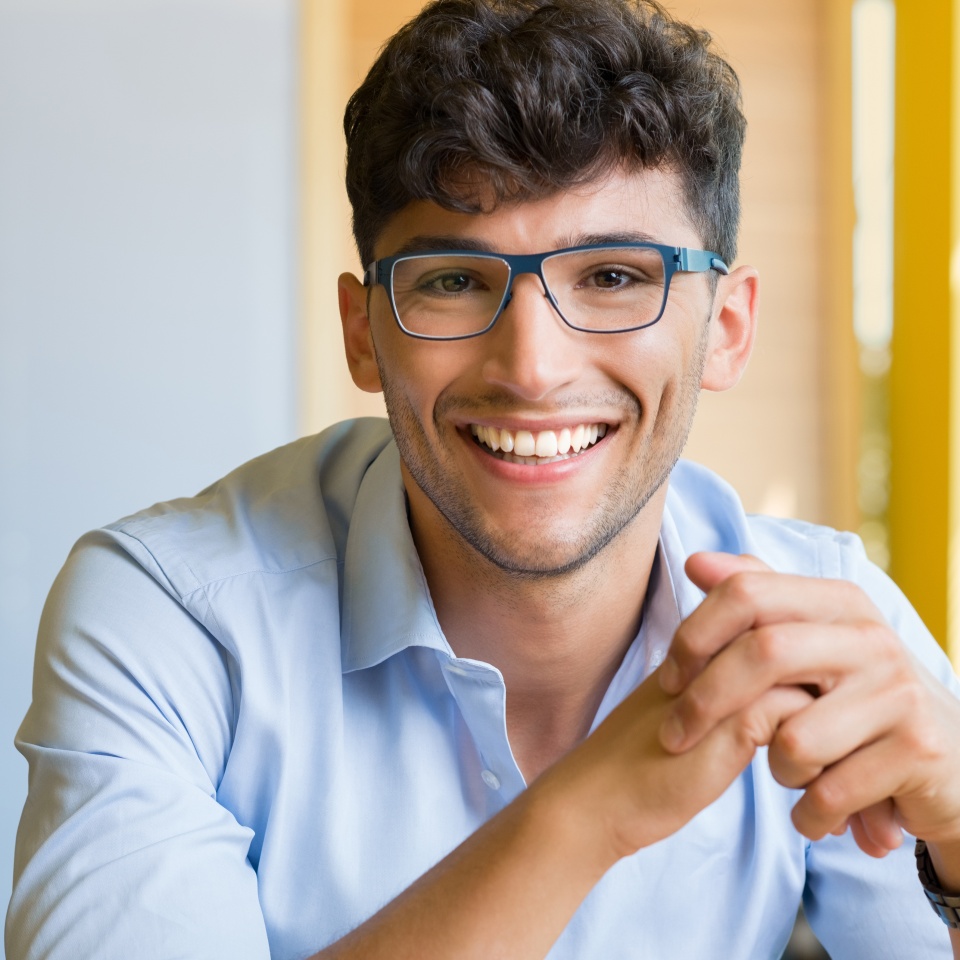Closeup shot of young man wearing spectacle. Portrait of a guy with shirt and eyeglasses looking at camera indoor. Handsome smiling young man wearing blue spectacle.