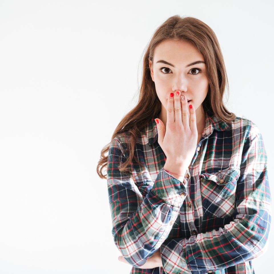 Happy amazed young woman covered her mouth by hand over white background