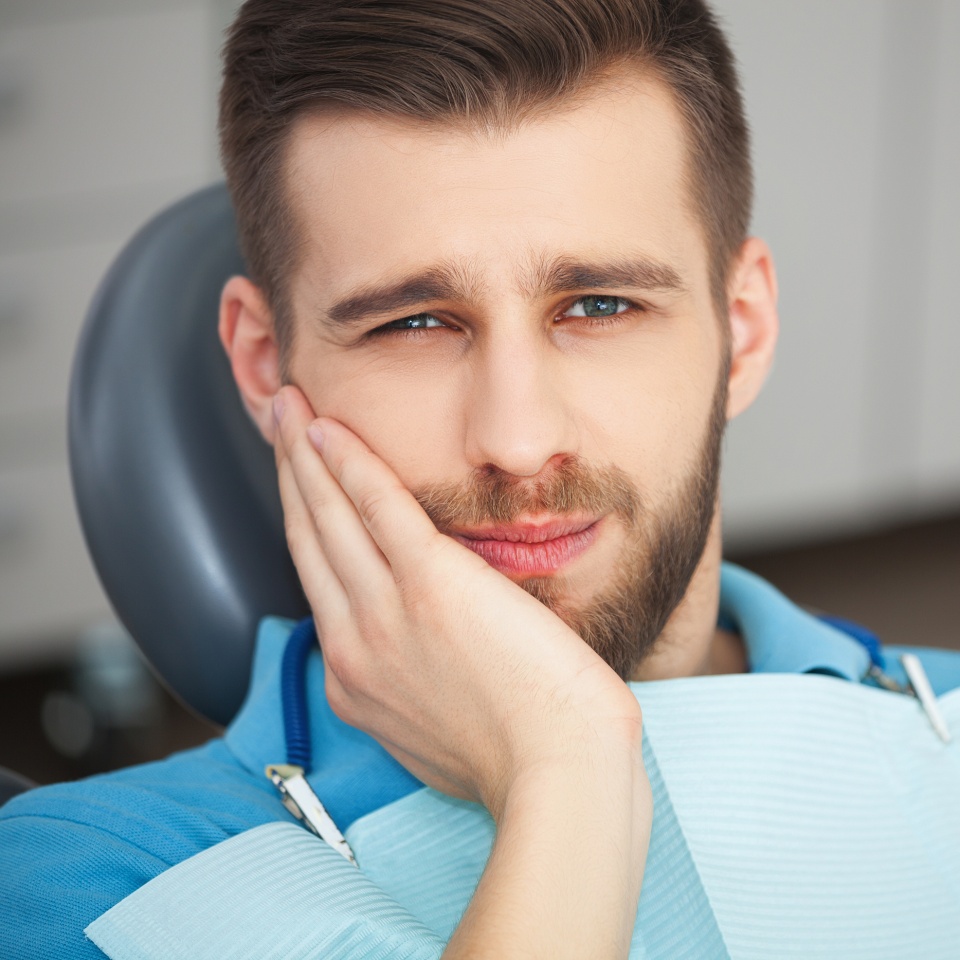 Shot of a young man with tooth pain while sitting in a dentist's chair.