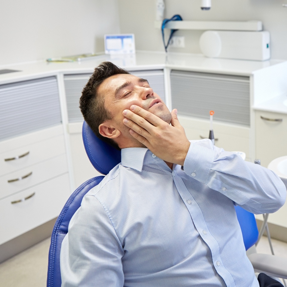 people, medicine, stomatology and health care concept - unhappy male patient having toothache sitting on dental chair at clinic office