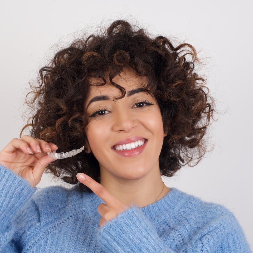 Young beautiful Arab woman holding an invisible aligner braces against white studio background and pointing at it. Dental healthcare concept.