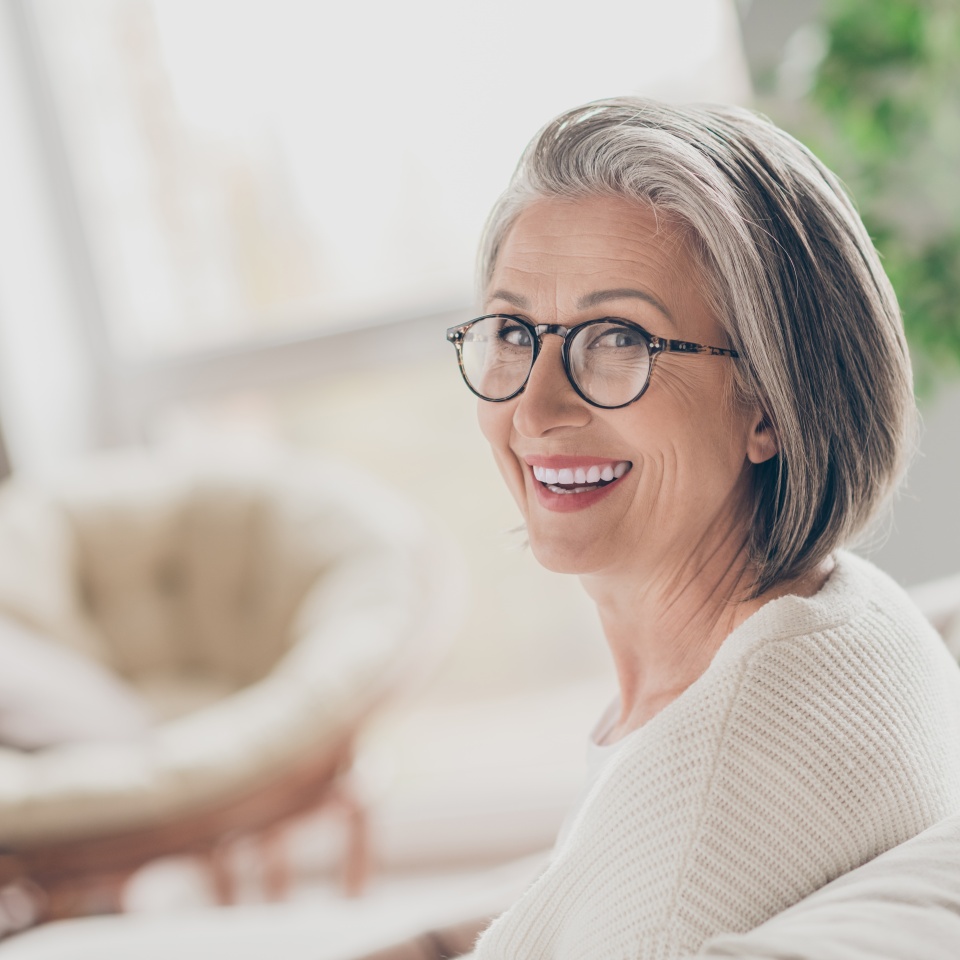 Photo of charming good mood elderly lady wear white cardigan spectacles smiling indoors apartment room