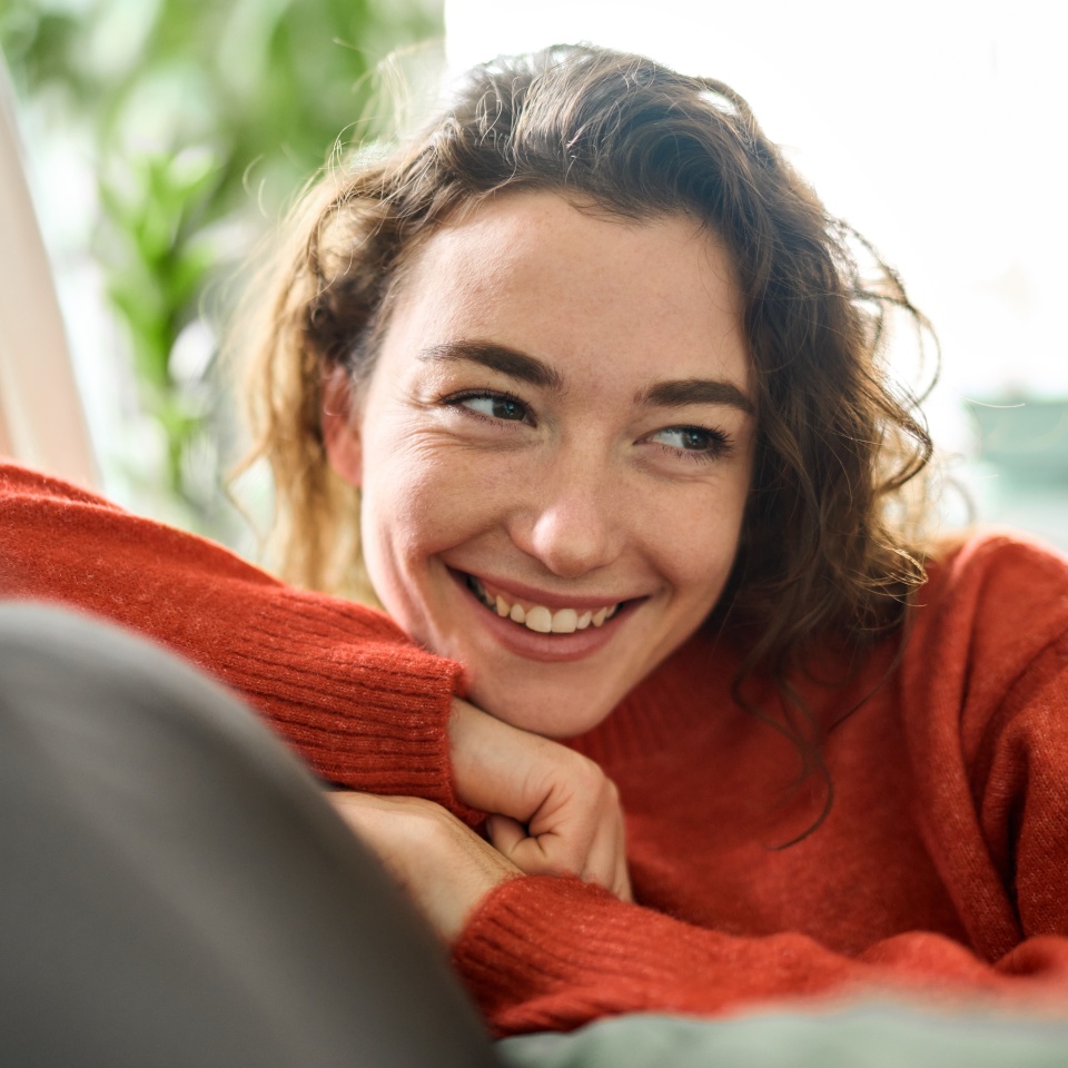 Happy relaxed calm beautiful lady enjoying comfort thinking or good on soft sofa looking away. Young smiling pretty curly woman relaxing sitting on couch at home and dreaming. Close up.