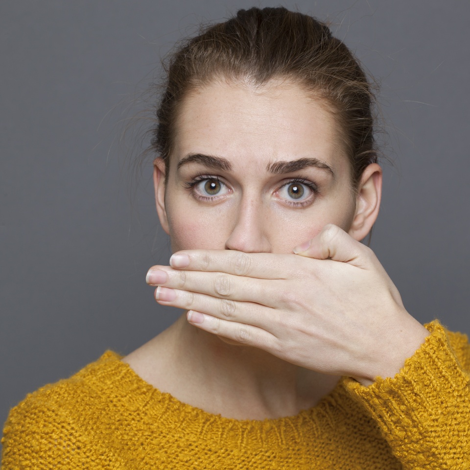 negative feelings concept - portrait of surprised beautiful 20s girl covering her mouth for bad breath or taboo,studio shot on gray background