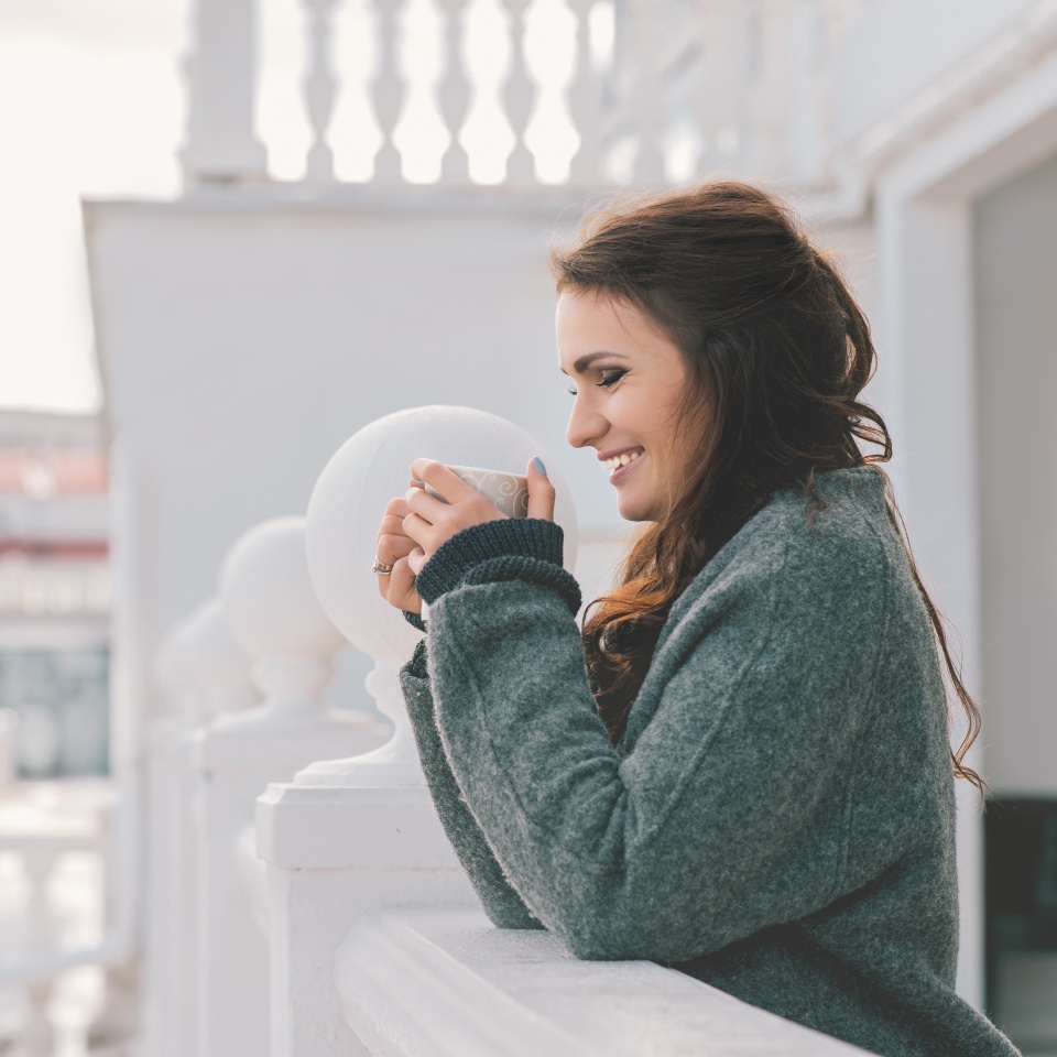 Beautiful smiling woman relaxing and drinking coffee on the balcony in the morning