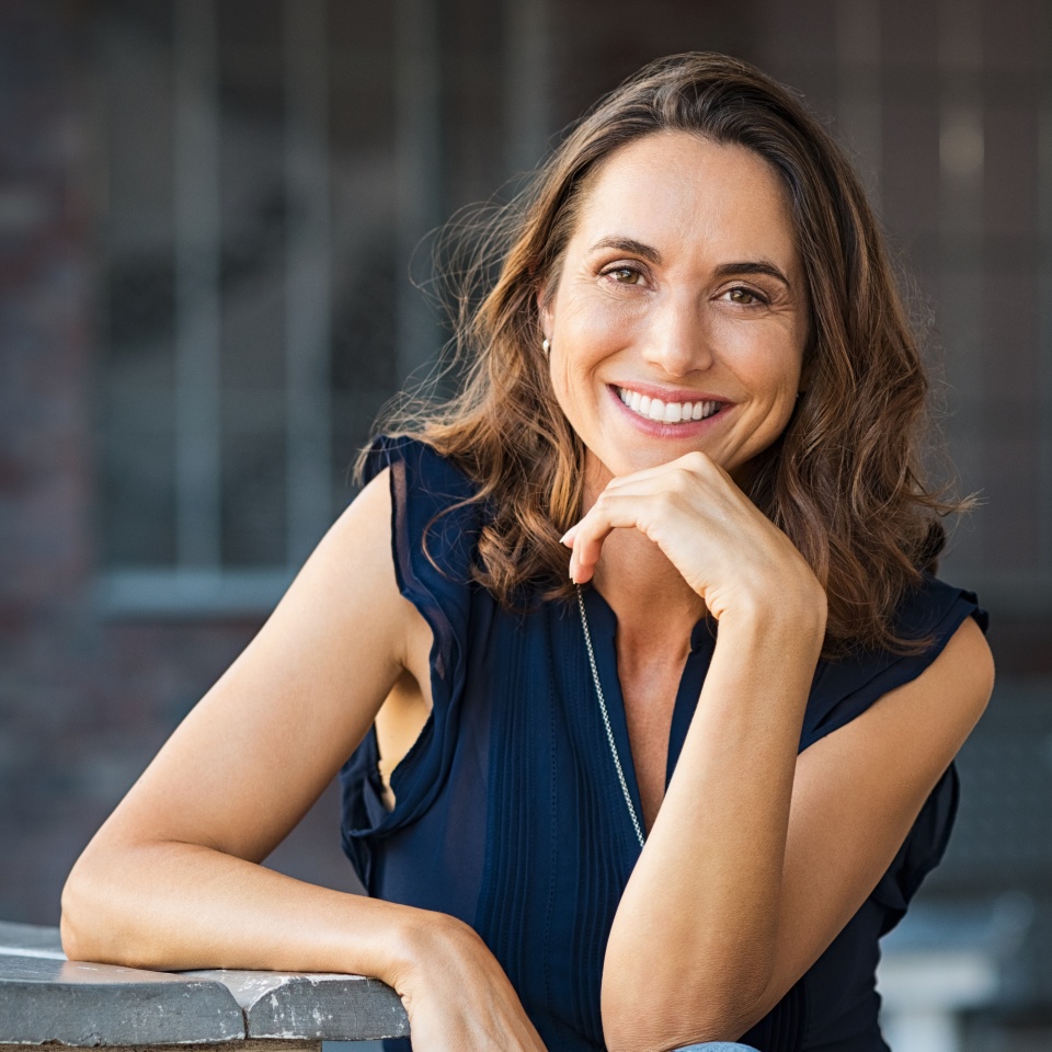 Portrait of beautiful mature woman sitting at coffee shop. Happy hispanic smiling woman sitting on a bench in outdoor cafeteria looking at camera. Portrait of carefree woman relaxing on bench.