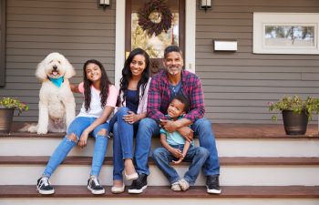 Family With Children And Pet Dog Sit On Steps Of Home